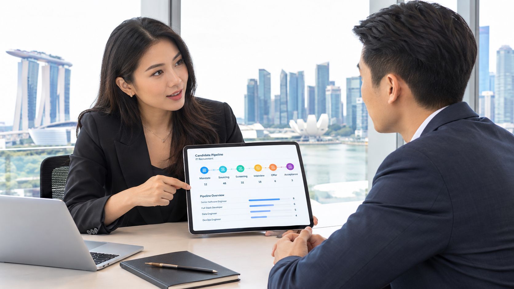 A professional business woman discussing an IT recruitment pipeline presentation on a tablet with her male colleague.